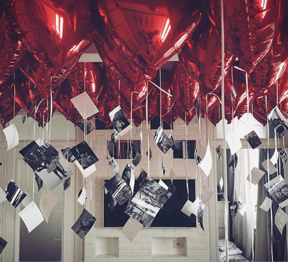 Valentine's day decoration in a room featuring red heart foil balloons with hanging photos. 