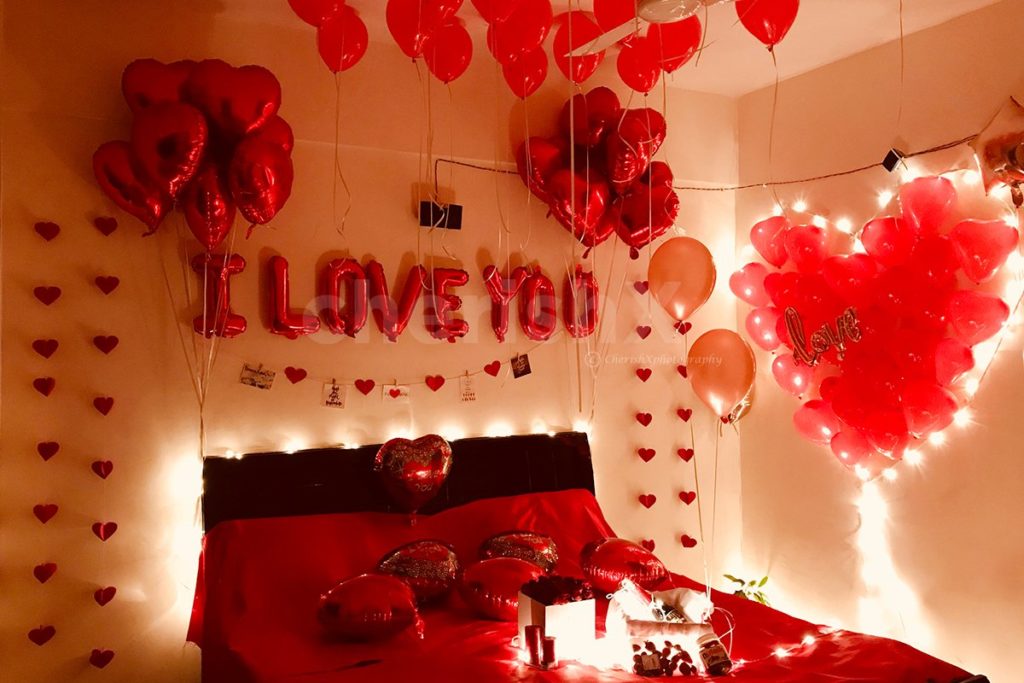 Valentine's day decorations in room featuring heart shaped foil balloons, I love You letter foil balloons, and heart shaped red balloons. 