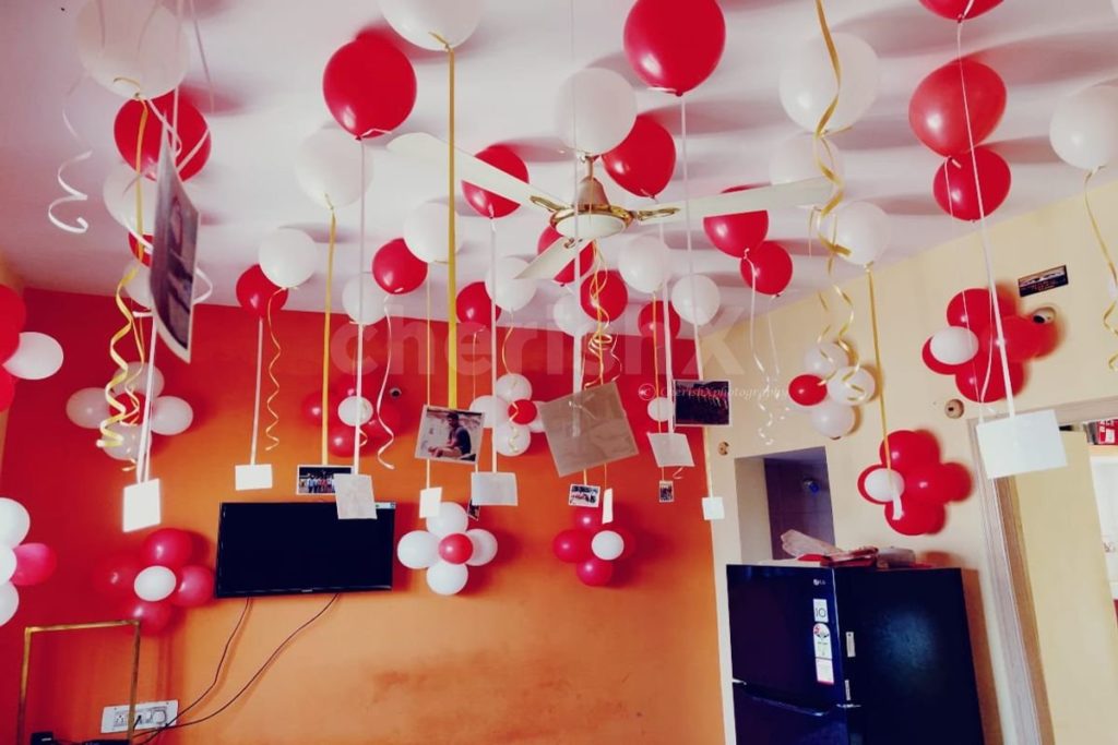 Valentine's day decoration in room featuring hanging white and red balloons along with photographs. 
