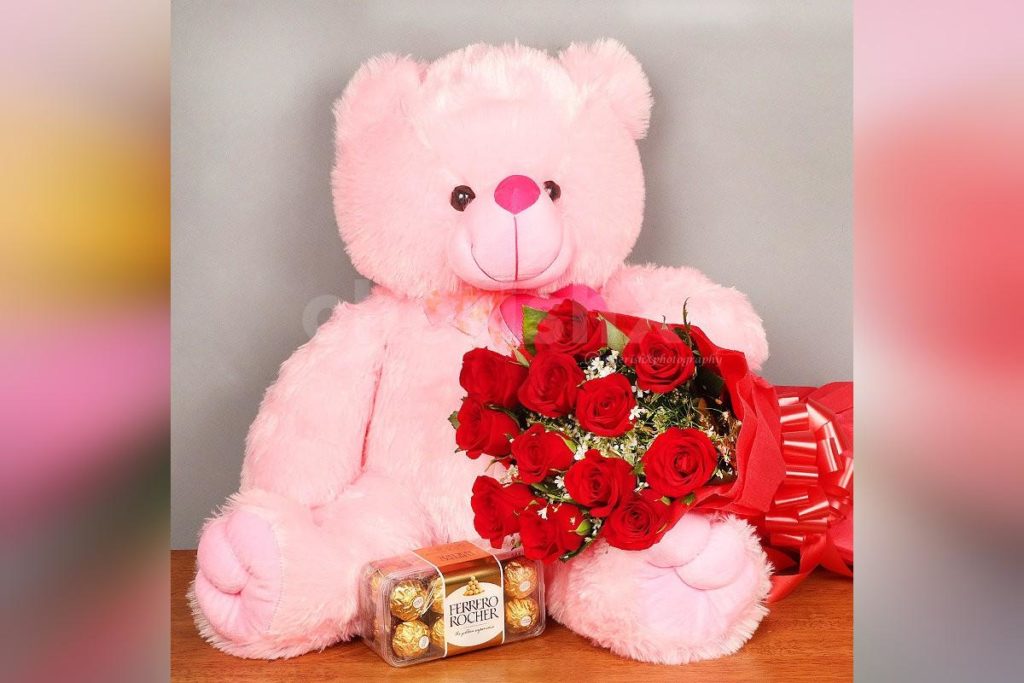 Hug day special gift featuring a pink teddy bear along with a a bouquet of red roses and a box of chocolates
