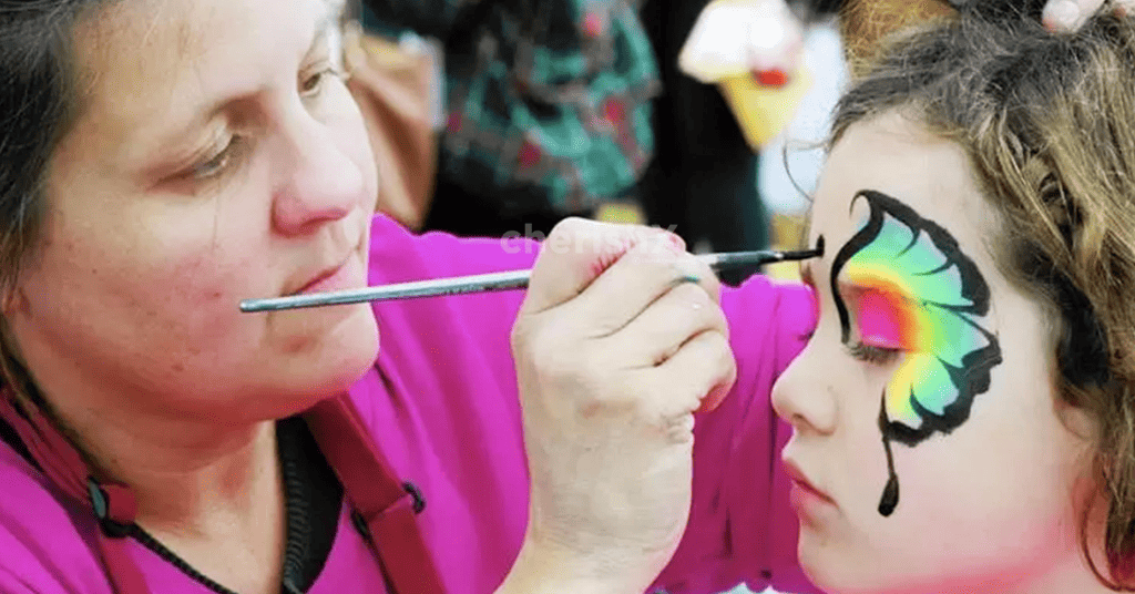 A face paint artist on a kid's birthday making a pretty butterfly near the child's eye