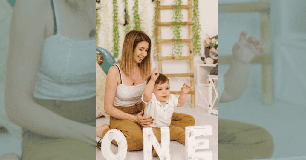 An indoor birthday photoshoot: Child on mother's lap with 'ONE' block letters."