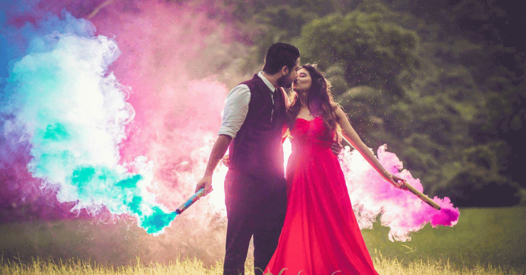 A couple kissing each other while holding color bombs in their hands for a photograph